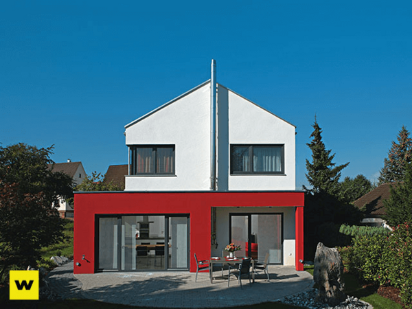 Modernes Einfamilienhaus mit roter Fassade, großen Fenstern und Garten bei blauem Himmel.