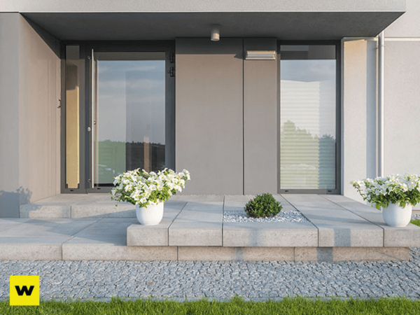 Moderner Hauseingang mit großen Fenstern, Blumen in weißen Töpfen und gepflegtem Vorgarten.